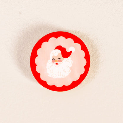Add festive charm to your decor with The Darling Effect's Holly Jolly Santa Wood Enamel Coaster, featuring a round design with a red border and cartoon Santa Claus face—perfect for any holiday coaster set.