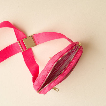 The Darling Effect's Hot Pink Urban Check Belt Bag is a chic woven vegan leather accessory with a gold buckle, two zippered compartments, and striped fabric lining—perfect for any occasion. Shown open on a light beige surface.