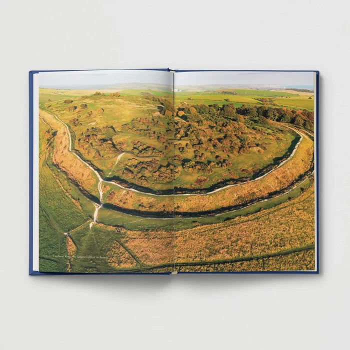 Aerial view of lush green hills from “Ancient Britain For Modern Folk” book by Hoxton Mini Press, hardcover open on display.