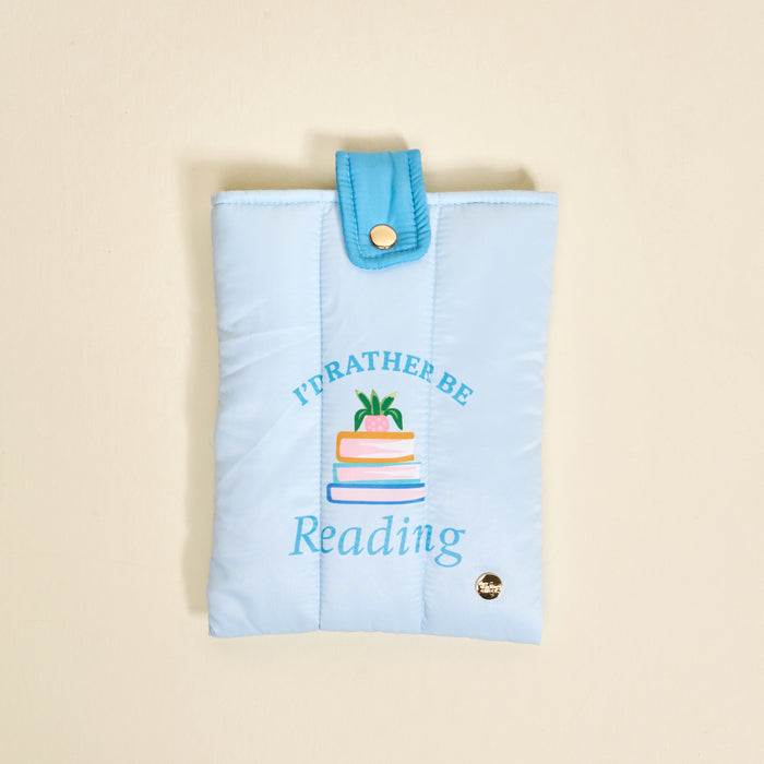 The Darling Effect's "I'd Rather Be Reading Book Cover" in light blue polyester features a quilted design, snap closure, vibrant stacked books with a plant, and protects your books in cute style.