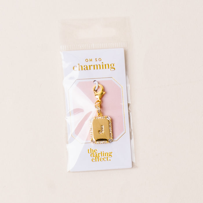 The-darling-effect J Jewelry Charm Initial Letter Gold features a gold-plated brass charm with a rhinestone-studded J, presented on an OH SO charming card and packaged in a clear plastic bag—perfect for personalized style.