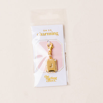 The-darling-effect J Jewelry Charm Initial Letter Gold features a gold-plated brass charm with a rhinestone-studded J, presented on an OH SO charming card and packaged in a clear plastic bag—perfect for personalized style.