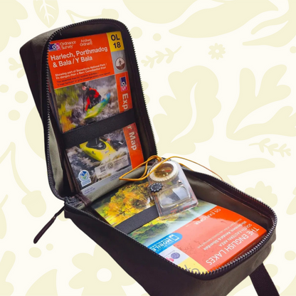 Forager Provisions LTD green waxed canvas map case open on a windowsill with maps, a compass, and binoculars nearby.