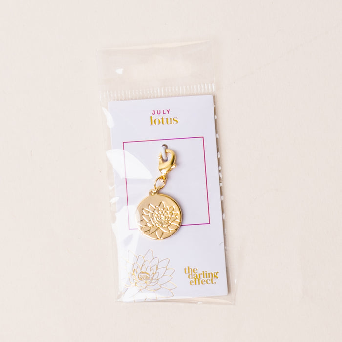 The July Jewelry Birth Flower Charm Gold by the-darling-effect comes on a card labeled JULY lotus in a clear plastic sleeve—a thoughtful gift for personalized jewelry lovers.