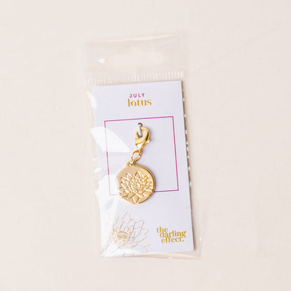 The July Jewelry Birth Flower Charm Gold by the-darling-effect comes on a card labeled JULY lotus in a clear plastic sleeve—a thoughtful gift for personalized jewelry lovers.