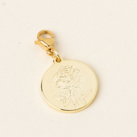 The-darling-effect's June Jewelry Birth Flower Charm Gold is a round gold pendant with an engraved rose and leaves, attached to a gold lobster clasp. This meaningful charm is perfect for lovers of personalized jewelry. Set on a plain light background.