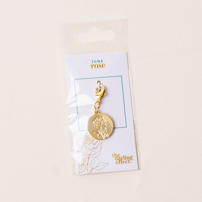 The June Jewelry Birth Flower Charm Gold by the-darling-effect features an engraved rose on a gold charm, attached to a "June rose" card and packaged in a clear plastic sleeve with a cream background.