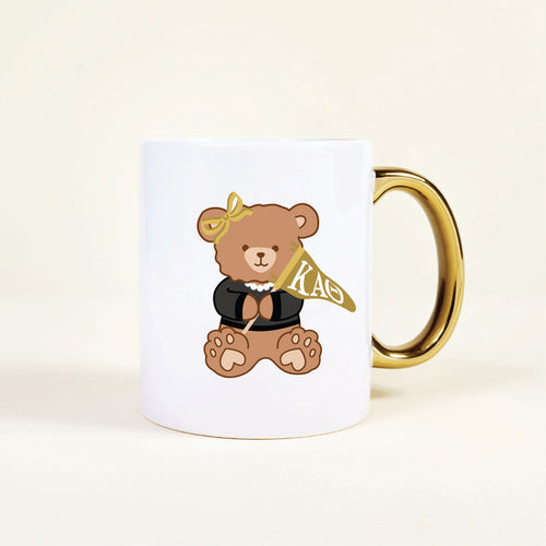 The Darling Effect’s Kappa Alpha Theta 11 oz Cozy Cute Ceramic Mug features a charming teddy bear in a black top, pearl necklace, yellow bow, and gold handle, holding a yellow KAO flag—perfect for sorority members.
