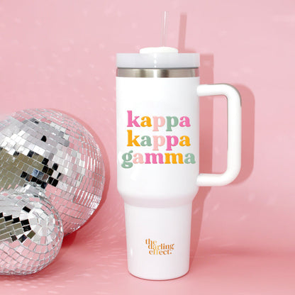 The Kappa Kappa Gamma 40 oz Take Me Everywhere White Tumbler by The Darling Effect, featuring a handle and straw, sits next to a disco ball on a pink background with "kappa kappa gamma" in colorful letters and the brand in gold at the bottom.