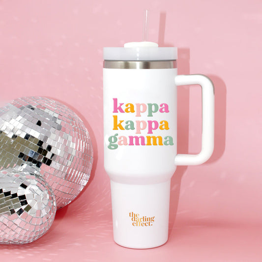 The Kappa Kappa Gamma 40 oz Take Me Everywhere White Tumbler by The Darling Effect, featuring a handle and straw, sits next to a disco ball on a pink background with "kappa kappa gamma" in colorful letters and the brand in gold at the bottom.
