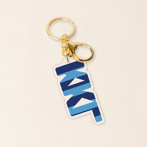 The Darling Effect’s Kappa Kappa Gamma Stripes Acrylic Keychain features a gold ring and a blue-and-white striped charm with bold, overlapping NKI text—ideal for sorority members or as a thoughtful KKG gift. Shown on a light beige background.