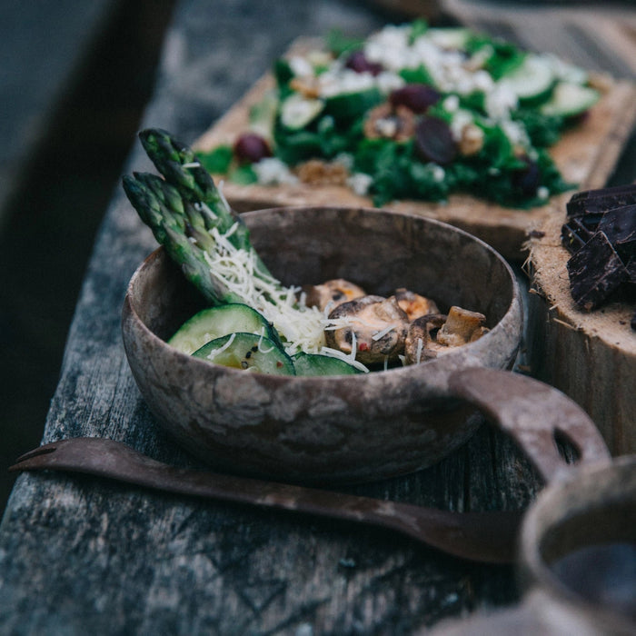 Rustic brown Kupilka 55 Soup Bowl with asparagus, mushrooms, cucumber, and cheese on wooden table – healthy soup meal photo.
