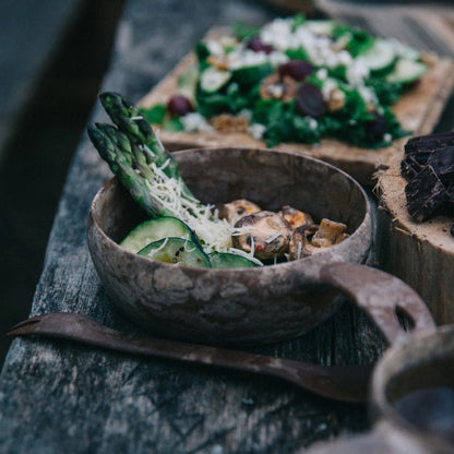 Rustic brown Kupilka 55 Soup Bowl with asparagus, mushrooms, cucumber, and cheese on wooden table – healthy soup meal photo.