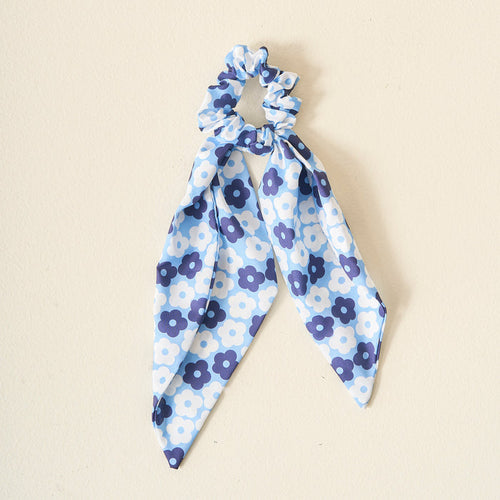 The Darling Effect's Light Blue Game Day Hair Scarf with Scrunchie features blue and white florals and two scarf-like tails, perfect for showcasing school colors, displayed on a simple light background.