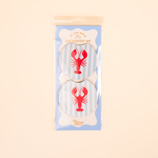 The Darling Effect Lobster On the Road Car Coaster Set includes two round absorbent coasters with blue stripes and red lobster designs, packaged in a clear bag with a light blue card—perfect for your car cup holder collection.