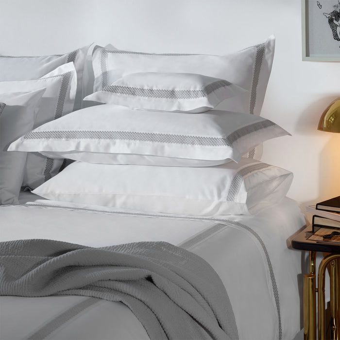 Stack of Luis-White-Grey pillowcases on a bed in a bedroom setting.