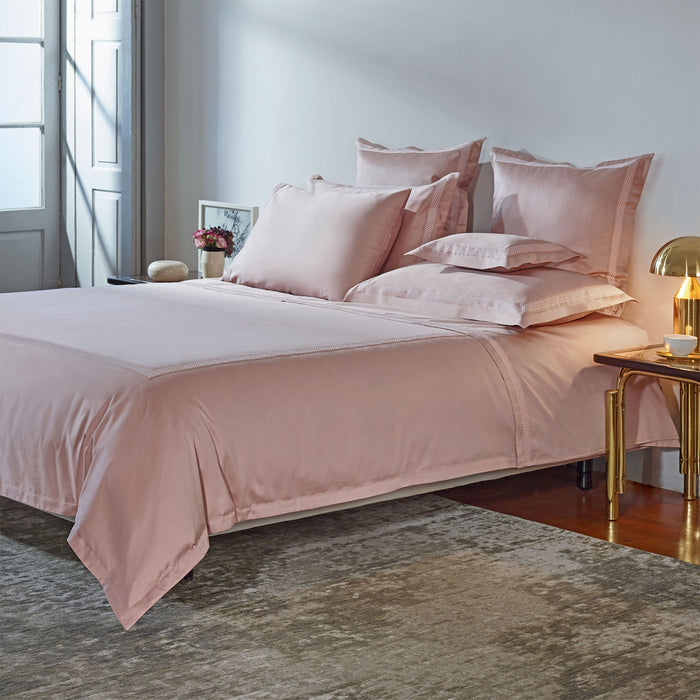 Luis-CharmPink duvet cover and pillowcase sham on a bed in a bedroom with a side table and lamp.