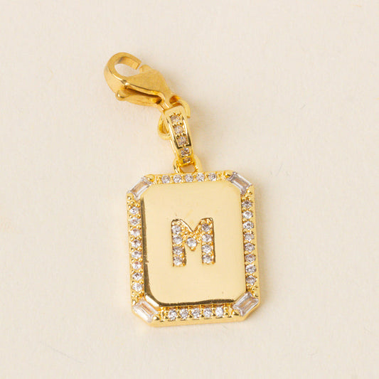 The-darling-effect M Jewelry Charm Initial Letter Gold features a rectangular, gold-plated brass pendant with a diamond-studded border, an M center, and gold lobster clasp for a personalized touch.