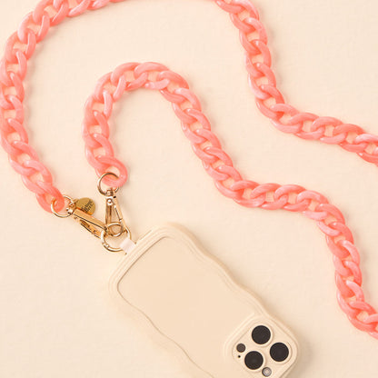 The-darling-effect Marble Bubblegum Hold the Phone Crossbody Chain, featuring a chunky light pink design with gold hardware, is attached to a white wavy edge phone case and displayed on a cream-colored surface.
