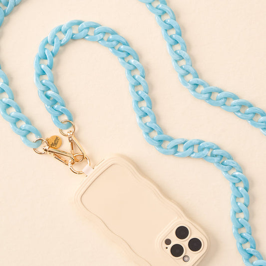 The Marble Ocean Blue Hold the Phone Crossbody Chain by the-darling-effect, featuring gold clasps, is attached to a beige wavy-edged phone case and displayed on a light surface.