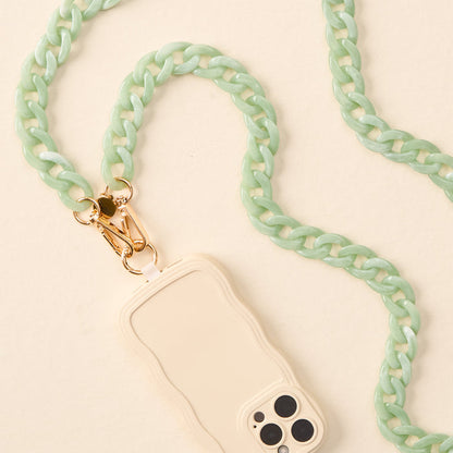 A cream smartphone with a wavy-edge case is paired with the-darling-effect’s Marble Seafoam Hold the Phone Crossbody Chain—a chunky mint strap with gold hardware—making it a chic accessory against a light beige background.