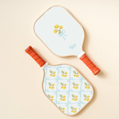 The-darling-effect's Marigold Lane Blue Pickleball Paddle features orange handles and lively designs: one with a yellow flower bouquet tied by a blue ribbon, the other with playful yellow flowers and blue ribbon patterns.