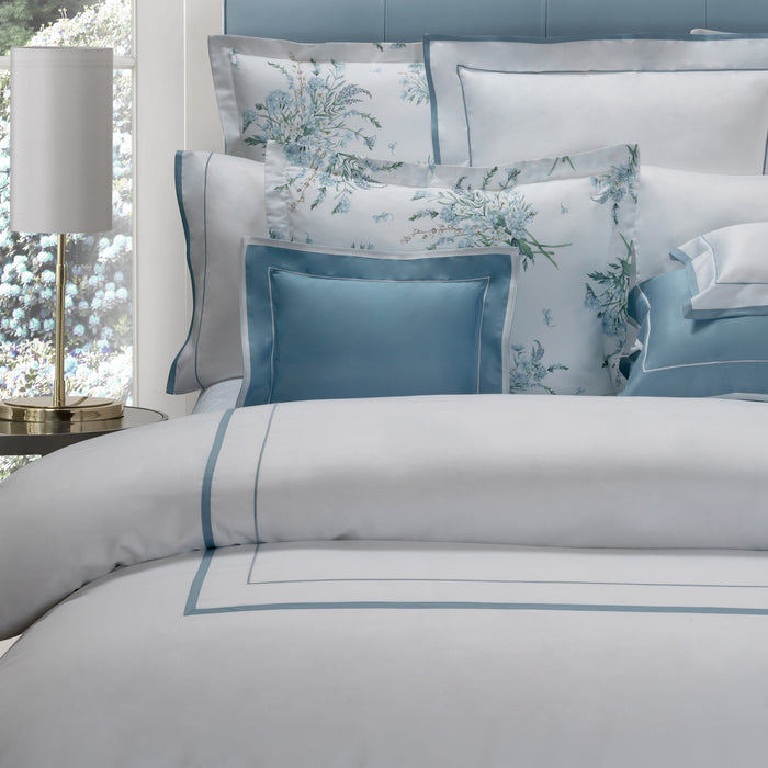 Mietta aquamarine and white pillowcase sham and duvet cover on a bed with a lamp in the background
