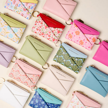 The Darling Effect’s Misty Blue Luxe Pocket Wallet is a compact, colorful zippered wallet with a keyring, featuring criss-cross design details and solid colors such as misty blue.