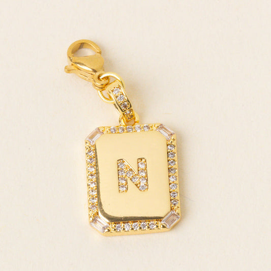 Gold rectangular pendant with a crystal-studded border and the letter N in the center, attached to a gold clasp with small crystals. This gold-plated brass charm is perfect for those who love Initial Letter Jewelry Charms and personalized jewelry.