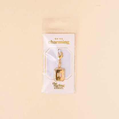 The-darling-effect N Jewelry Charm Initial Letter Gold features a gold-plated brass M encrusted with small gems and a lobster clasp, displayed on an OH SO charming card in clear packaging.