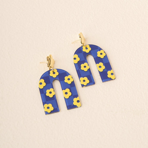 The Darling Effect Navy Yellow Game Day Acrylic Earrings feature arch-shaped acrylic with a blue background, yellow flower pattern, and gold stud accents—ideal for showing school spirit or adding flair to your game day look.