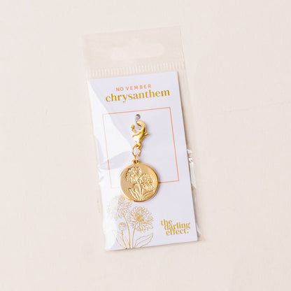 The-darling-effect November Jewelry Birth Flower Charm Gold features a chrysanthemum engraving and gold loop, mounted on a white NOVEMBER card. A meaningful gift, it's packaged in a clear sleeve.
