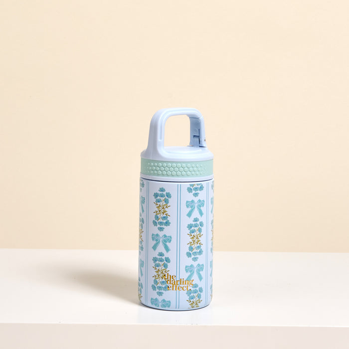 A petite Oh So Fancy Blue 6 oz Lil' Bitty Bottle by The Darling Effect features gold and blue floral patterns, "The Chai Edit" on the front, and a handle—perfect for hydration on the go, set against a beige background.