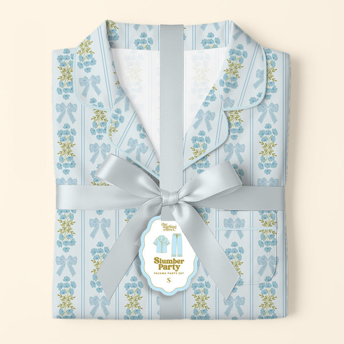 Folded Oh So Fancy Blue Slumber Party Pajama Pants Set by The Darling Effect, featuring a floral and bow design on ultra-soft fabric, tied with a satin ribbon and a “Slumber Party Pajama Party Kit” tag on a soft cream background.