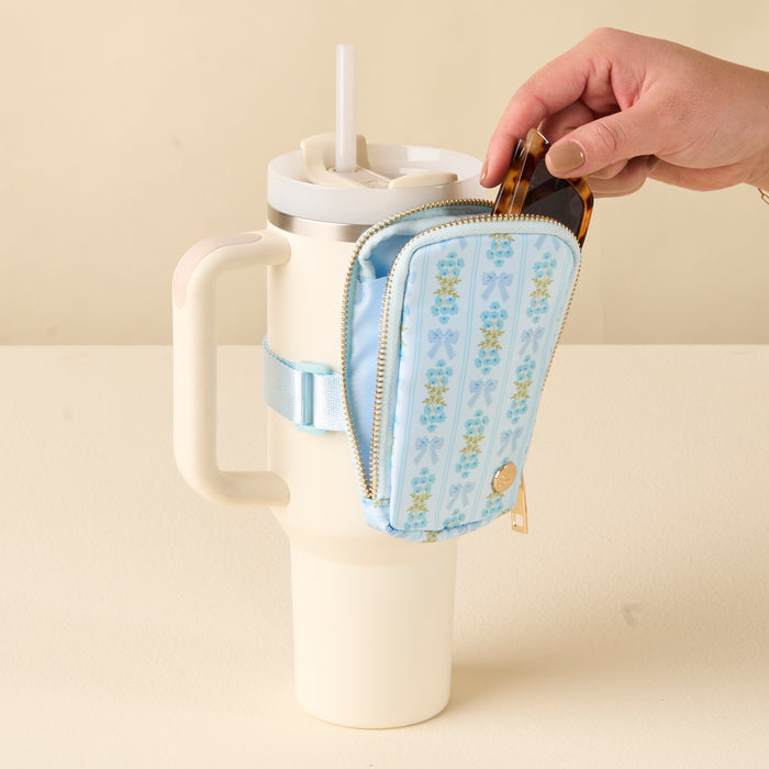 A hand puts sunglasses in the-darling-effect's Oh So Fancy Blue Tumbler Fanny Pack, which is attached to a cream travel mug with a straw.
