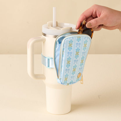 A hand puts sunglasses in the-darling-effect's Oh So Fancy Blue Tumbler Fanny Pack, which is attached to a cream travel mug with a straw.