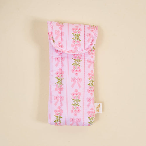 The Darling Effect’s Oh So Fancy Pink Puffy Sunglasses Case is a soft, rectangular case with a magnetic flap, featuring vertical pink bows and flowers on light pink, plus a side white tag.