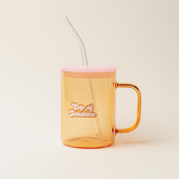 The Darling Effect’s Orange Cup of Sunshine Color Glass Mug with Handle features a transparent orange body, pink lid, clear bent straw, and “Cup of Sunshine” printed in white and orange on the front, set against a plain off-white background.