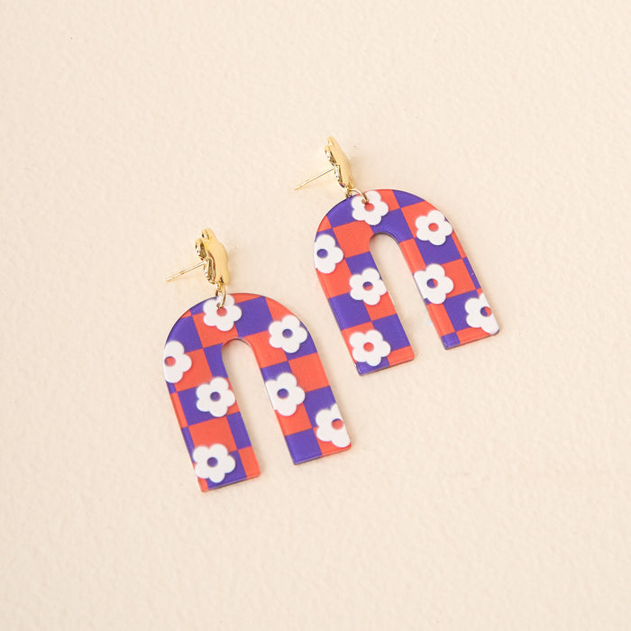 Orange Purple Game Day Acrylic Earrings by The Darling Effect feature an arch-shaped acrylic design with bold orange and purple checks, adorned with white flowers—perfect for adding playful school spirit to your game day look.