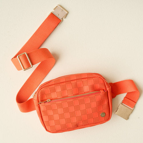 The Darling Effect’s Orange Urban Check Belt Bag features vegan leather, a woven design, matching adjustable strap, gold buckle, and front zip pocket—shown here against a light beige background.