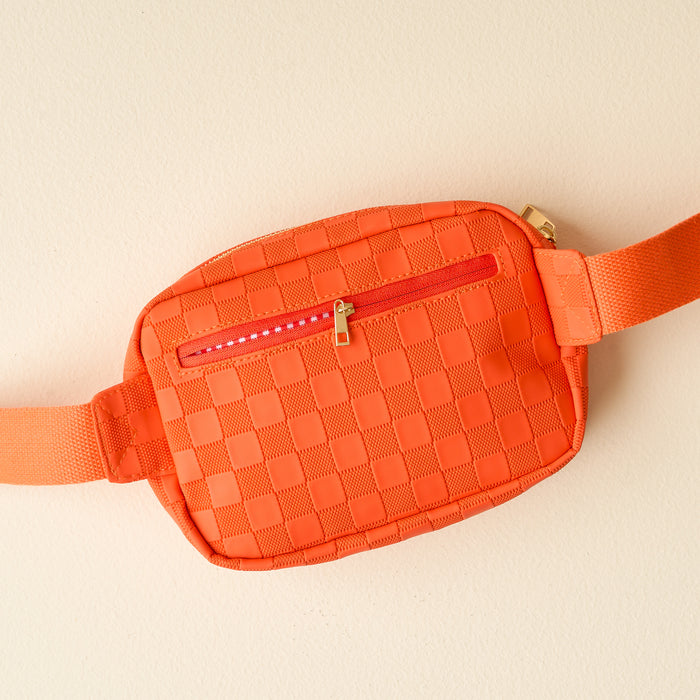 The Darling Effect’s Orange Urban Check Belt Bag features a front zipper pocket, matching adjustable strap, and vegan leather—making it a trendy accessory for any outfit. Displayed on a light beige surface.