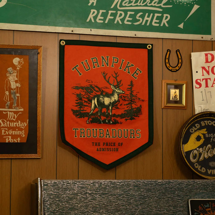 Forager Provisions LTD Oxford Pennant Turnpike Troubadours camp flag with a stag graphic on orange felt wall decor.