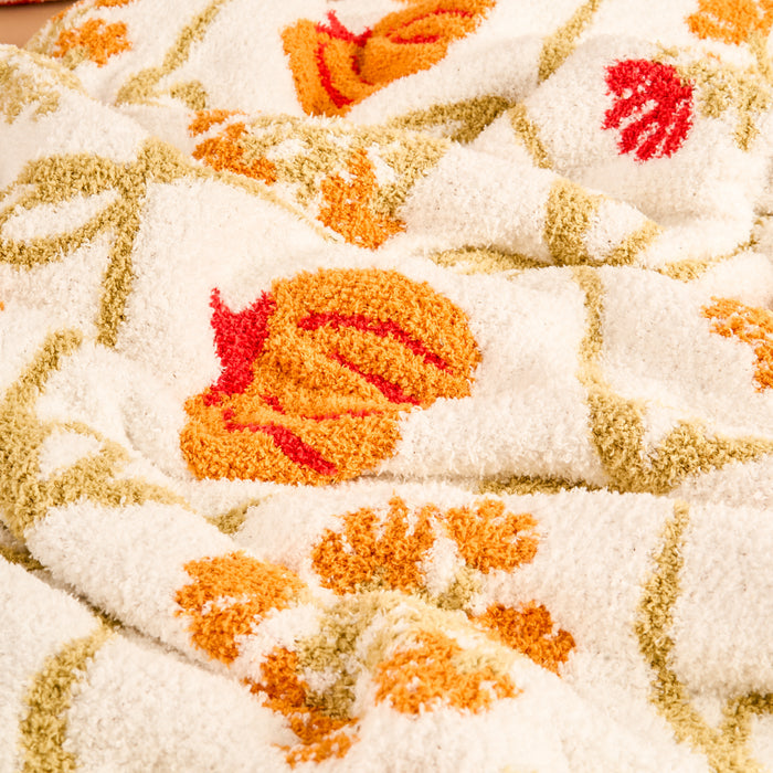 Close-up of The Darling Effect Patchwork Pumpkins Cozy Dreams Luxe Blanket, a soft white microfiber throw featuring textured surface with orange, yellow, and red pumpkin and floral patterns plus green stems.