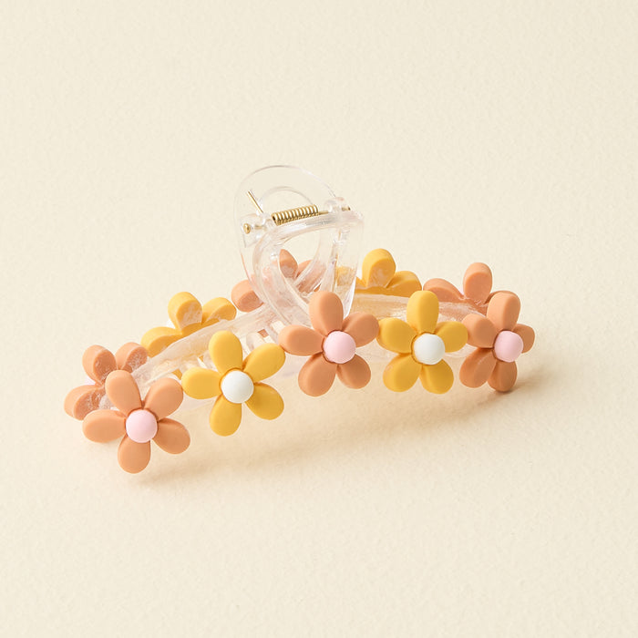 The Darling Effect's Peachy Daisy Claw Clip is a clear plastic hair accessory featuring alternating yellow and peach daisy-shaped flowers with pastel centers, perfect for adding a stylish pop against any cream background.