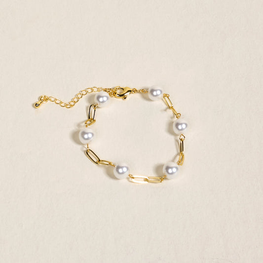 The Pearl Paperclip Bracelet Chain by The Darling Effect features gold paperclip-style links with white pearls, elegantly displayed on a light beige background.