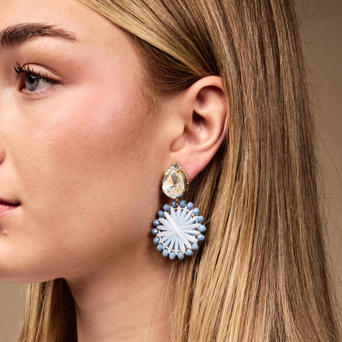 Close-up of a woman with straight blonde hair wearing The Darling Effect's Periwinkle Radiant Gem Earrings—lightweight, boho style with teardrop crystal and circular white and light blue design—perfect for everyday wear.