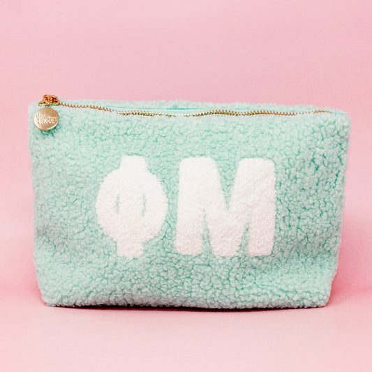 The Darling Effect's Phi Mu Aqua Teddy Letter Pouch features white Greek letters on light blue fuzzy fabric, a gold zipper charm, and is perfect as a cute carry-on accessory for Phi Mu or teddy pouch fans.
