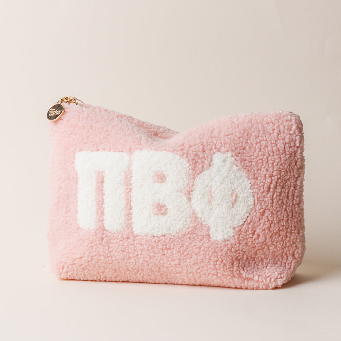 The Darling Effect Pi Beta Phi Blush Teddy Letter Pouch is a soft pink sherpa pouch with a gold zipper, round charm, and bold white ΠΒΦ letters—ideal as a stylish carry-on accessory.