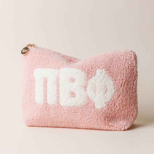 The Darling Effect Pi Beta Phi Blush Teddy Letter Pouch is a soft pink sherpa pouch with a gold zipper, round charm, and bold white ΠΒΦ letters—ideal as a stylish carry-on accessory.
