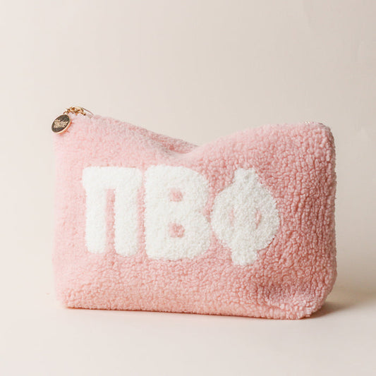 The Darling Effect Pi Beta Phi Blush Teddy Letter Pouch is a soft pink sherpa pouch with a gold zipper, round charm, and bold white ΠΒΦ letters—ideal as a stylish carry-on accessory.